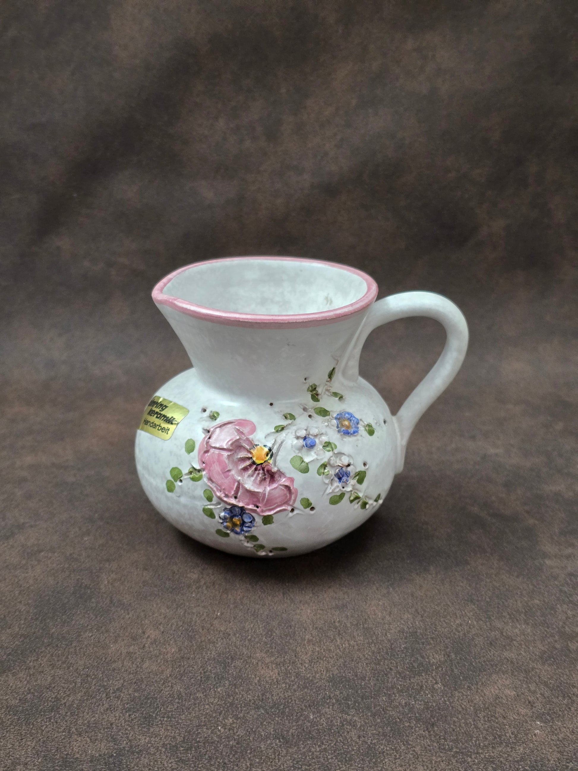 Handgefertigter Vintage-Dekokrug aus Ainring Keramik mit floralem Relief, matter Glasur und Originalaufkleber, deutsche Kunstkeramik der 1960er–1970er Jahre.
