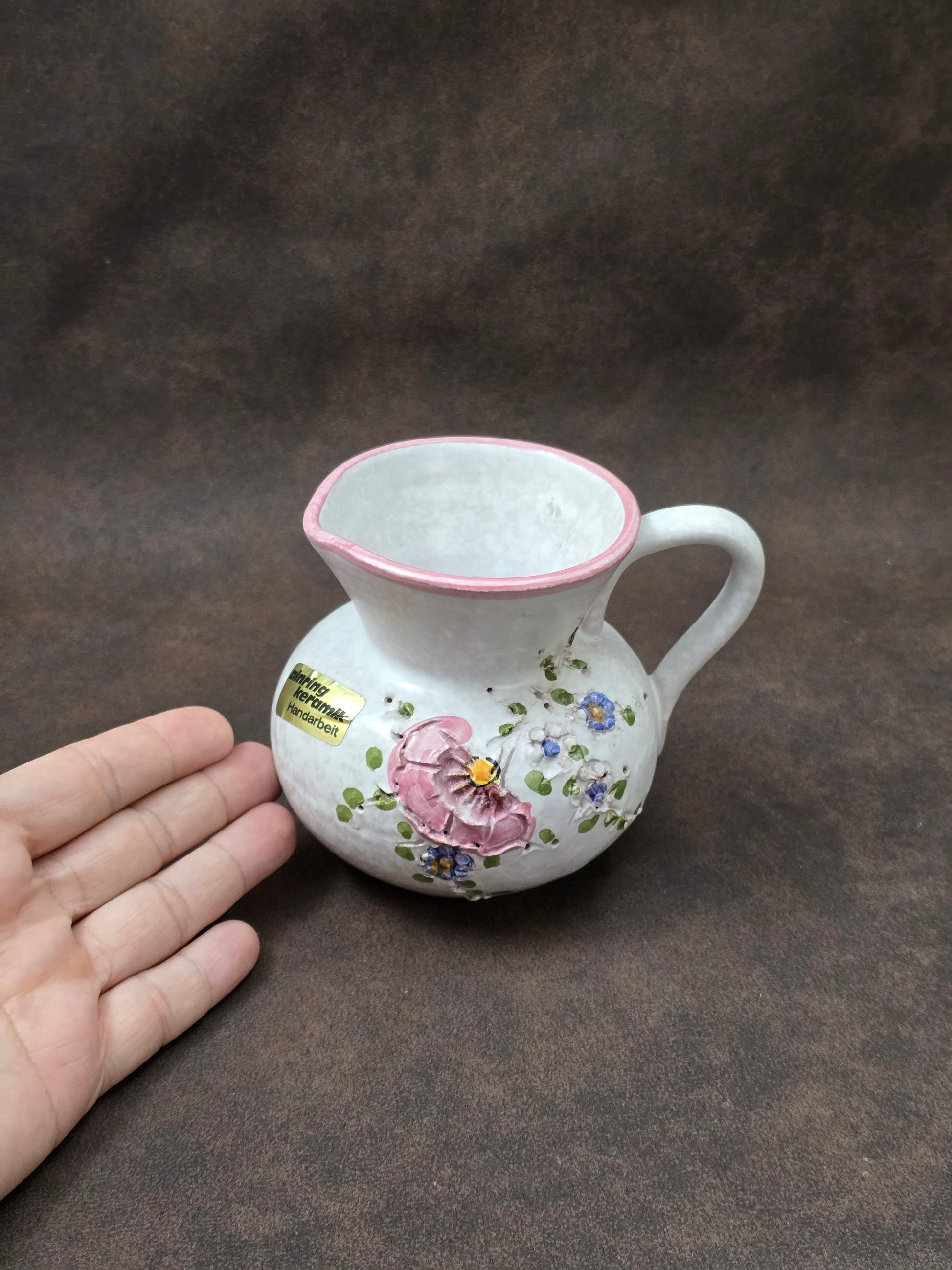 Handgefertigter Vintage-Dekokrug aus Ainring Keramik mit floralem Relief, matter Glasur und Originalaufkleber, deutsche Kunstkeramik der 1960er–1970er Jahre.