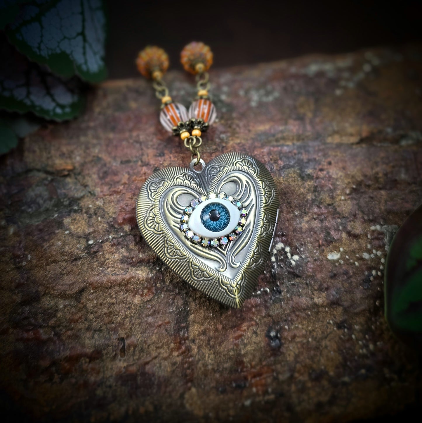Herzmedaillon-Kette mit skurrilem Auge & Strass. Orange & Bronze, handmade & einzigartig. Mit Hakenverschluss & geheimnisvollem Look. Für alle, die das Besondere lieben.