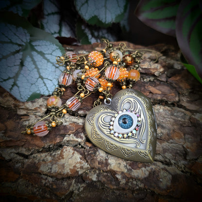Herzmedaillon-Kette mit skurrilem Auge & Strass. Orange & Bronze, handmade & einzigartig. Mit Hakenverschluss & geheimnisvollem Look. Für alle, die das Besondere lieben.