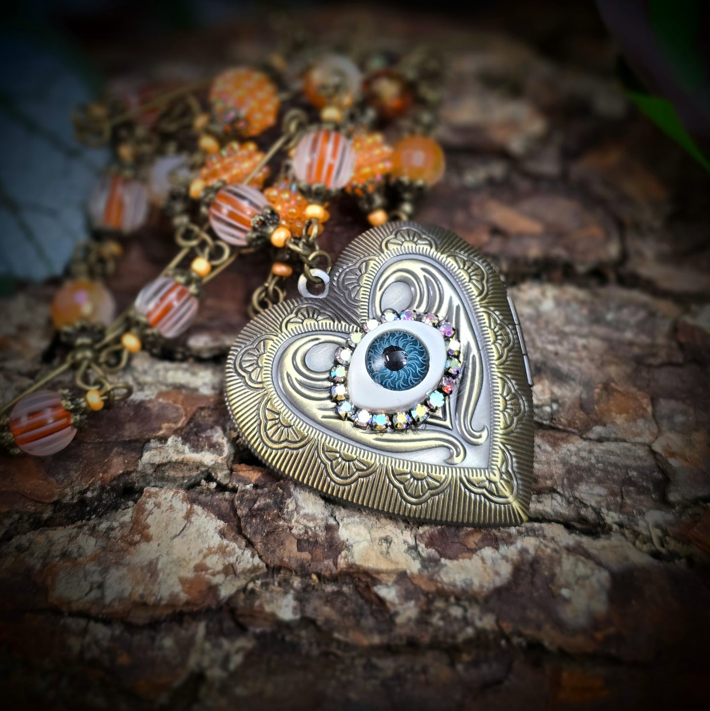 Herzmedaillon-Kette mit skurrilem Auge & Strass. Orange & Bronze, handmade & einzigartig. Mit Hakenverschluss & geheimnisvollem Look. Für alle, die das Besondere lieben.