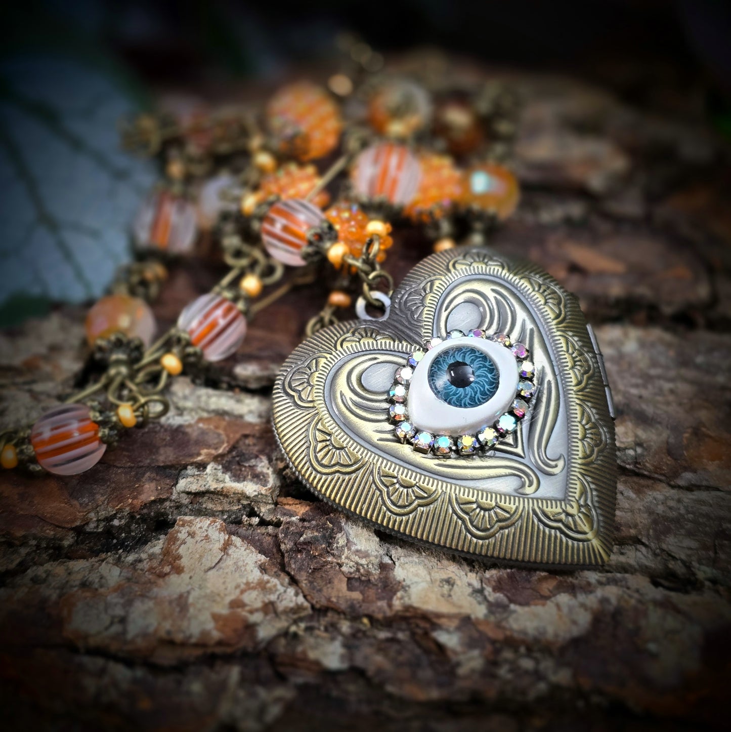 Herzmedaillon-Kette mit skurrilem Auge & Strass. Orange & Bronze, handmade & einzigartig. Mit Hakenverschluss & geheimnisvollem Look. Für alle, die das Besondere lieben.