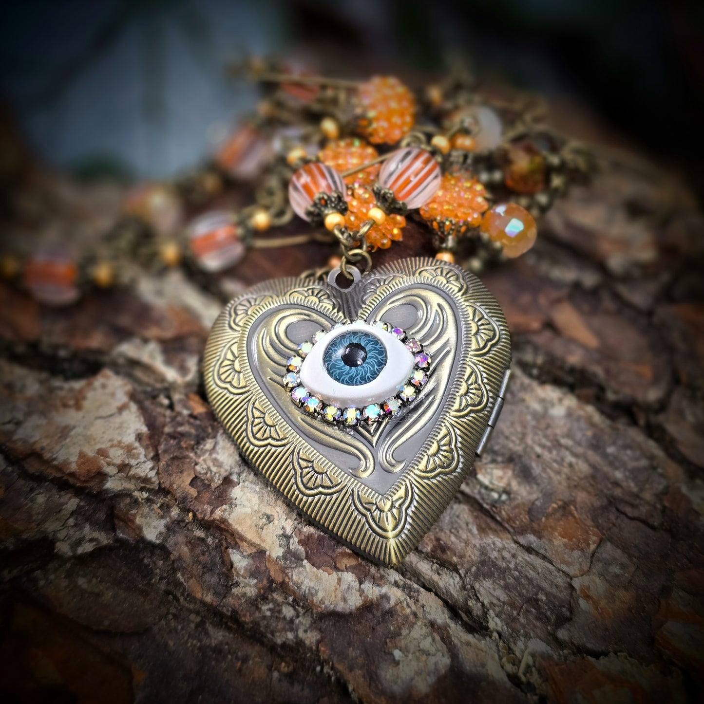 Herzmedaillon-Kette mit skurrilem Auge & Strass. Orange & Bronze, handmade & einzigartig. Mit Hakenverschluss & geheimnisvollem Look. Für alle, die das Besondere lieben.