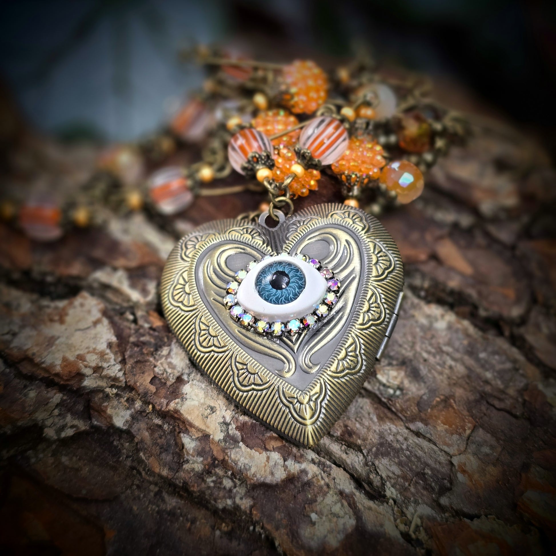 Herzmedaillon-Kette mit skurrilem Auge & Strass. Orange & Bronze, handmade & einzigartig. Mit Hakenverschluss & geheimnisvollem Look. Für alle, die das Besondere lieben.