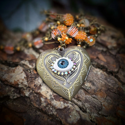 Herzmedaillon-Kette mit skurrilem Auge & Strass. Orange & Bronze, handmade & einzigartig. Mit Hakenverschluss & geheimnisvollem Look. Für alle, die das Besondere lieben.