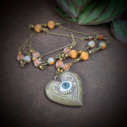 Herzmedaillon-Kette mit skurrilem Auge & Strass. Orange & Bronze, handmade & einzigartig. Mit Hakenverschluss & geheimnisvollem Look. Für alle, die das Besondere lieben.