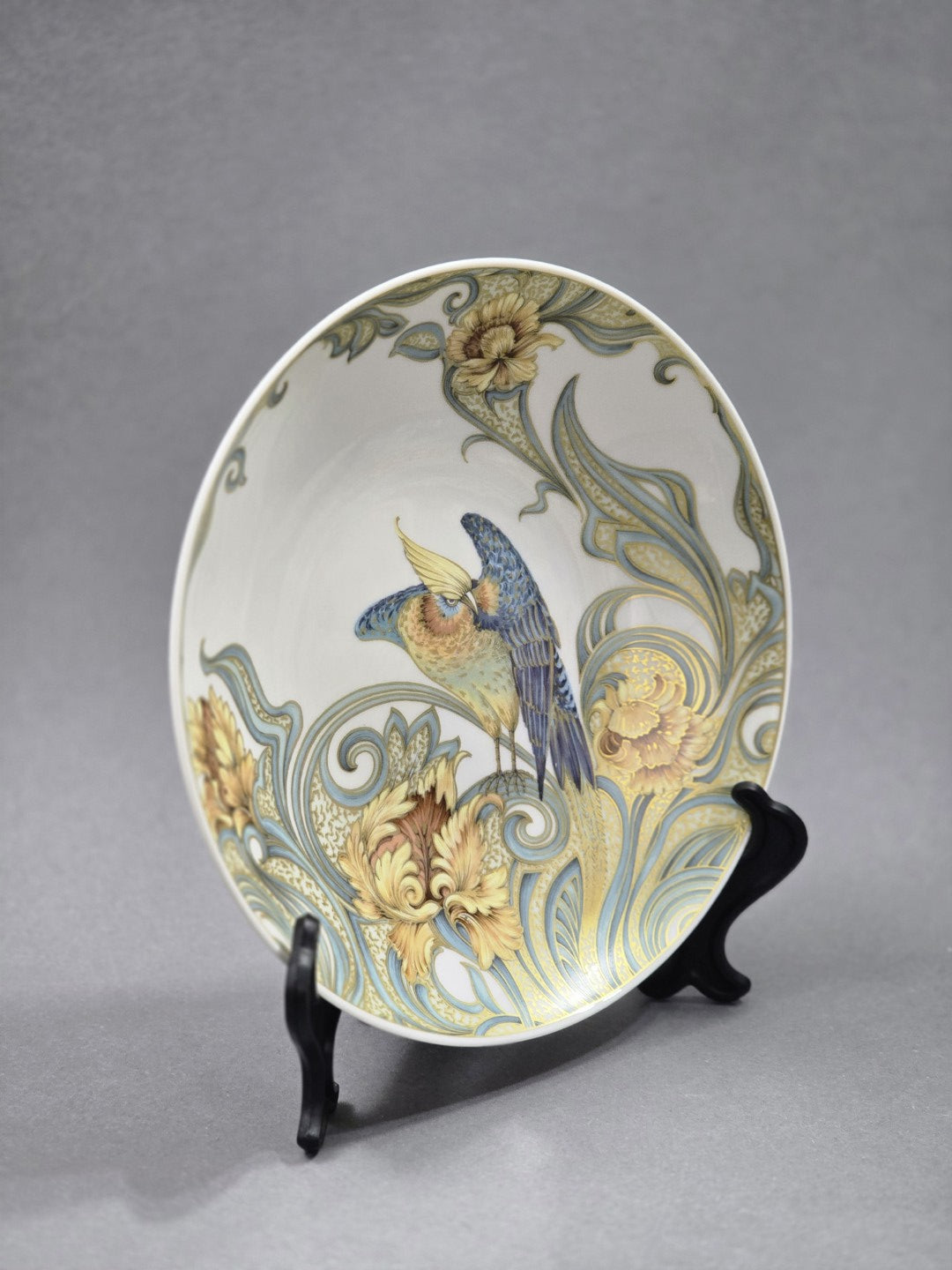 Vintage Kaiser Porzellanschale mit blau-goldenem Vogel- und Blumendekor, schräg von rechts fotografiert und auf schwarzem Ständer präsentiert