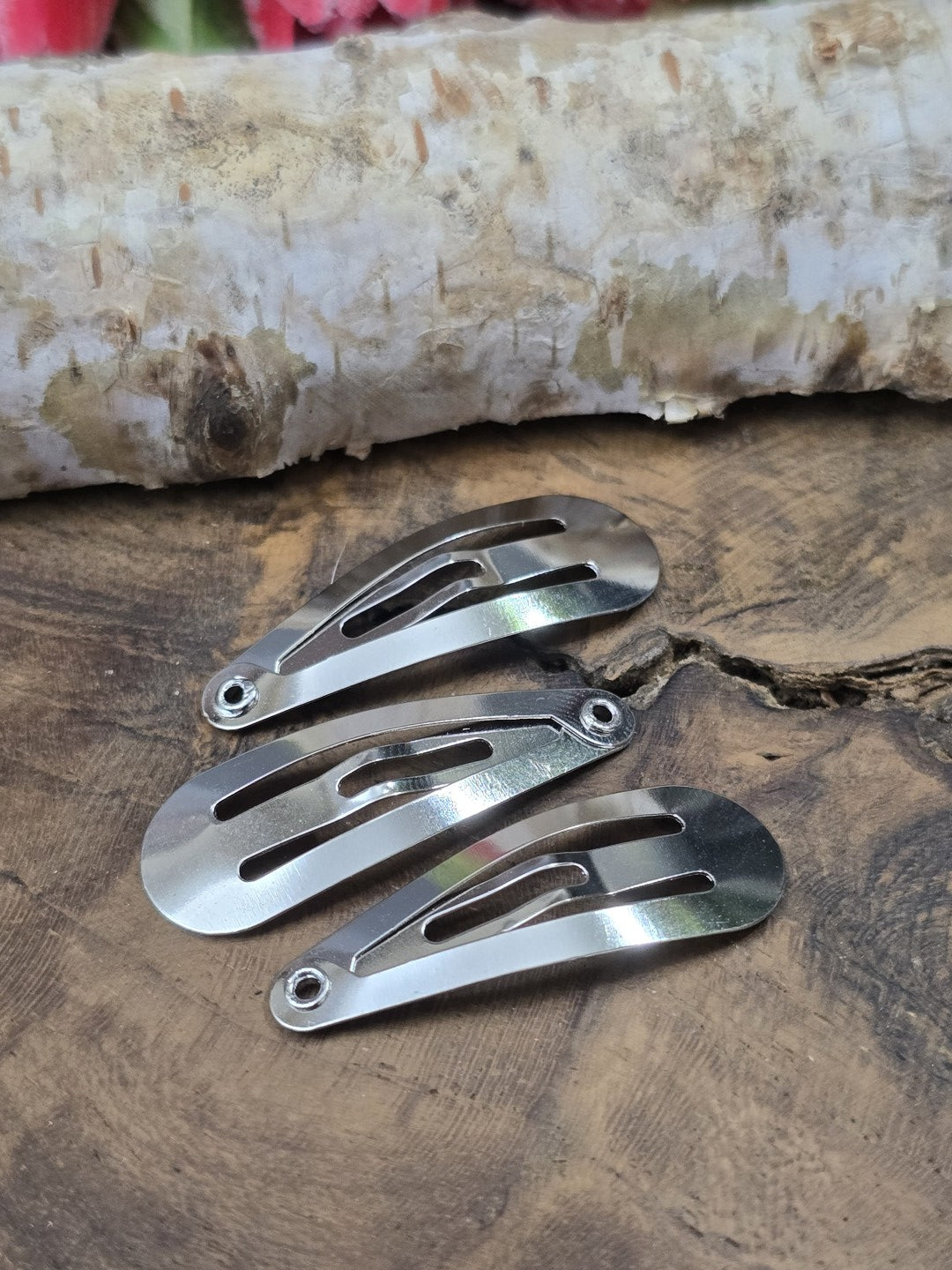 Drei geschlossene, silberne Haarspangen-Rohlinge (30 mm) aus Metall mit einer kleinen Öse an der Spitze flach liegend auf Holzgrund vor Birkenrinde.
