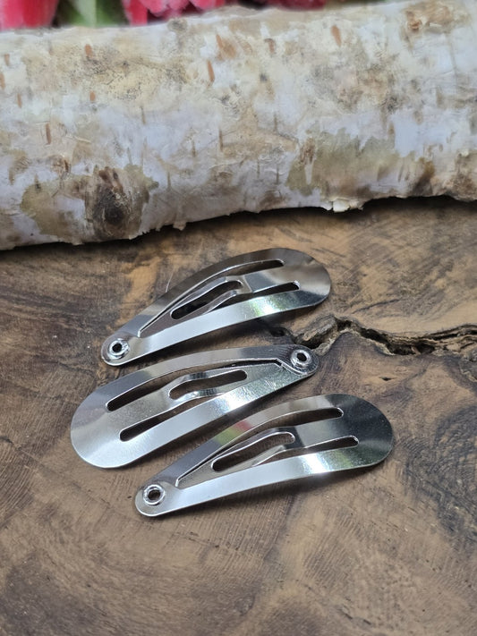 Drei geschlossene, silberne Haarspangen-Rohlinge (30 mm) aus Metall mit einer kleinen Öse an der Spitze flach liegend auf Holzgrund vor Birkenrinde.