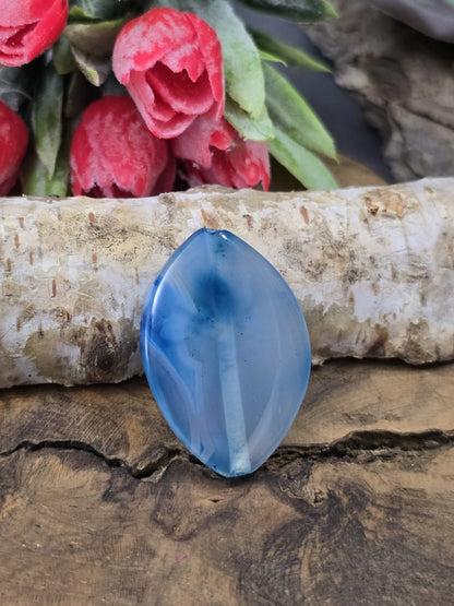 Große blaue Edelsteinperle aus Achat in marquiseförmiger Navette-Form auf Holz mit sanfter Bänderung im Stein.