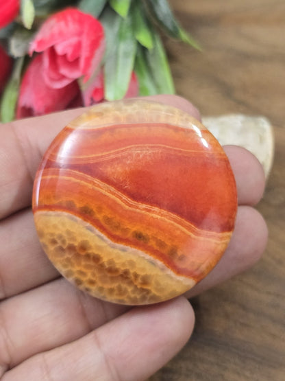 Polierte rot-orange Achatperle in Münzform auf der flachen Hand als Größenvorstellung für Schmuckkreationen.