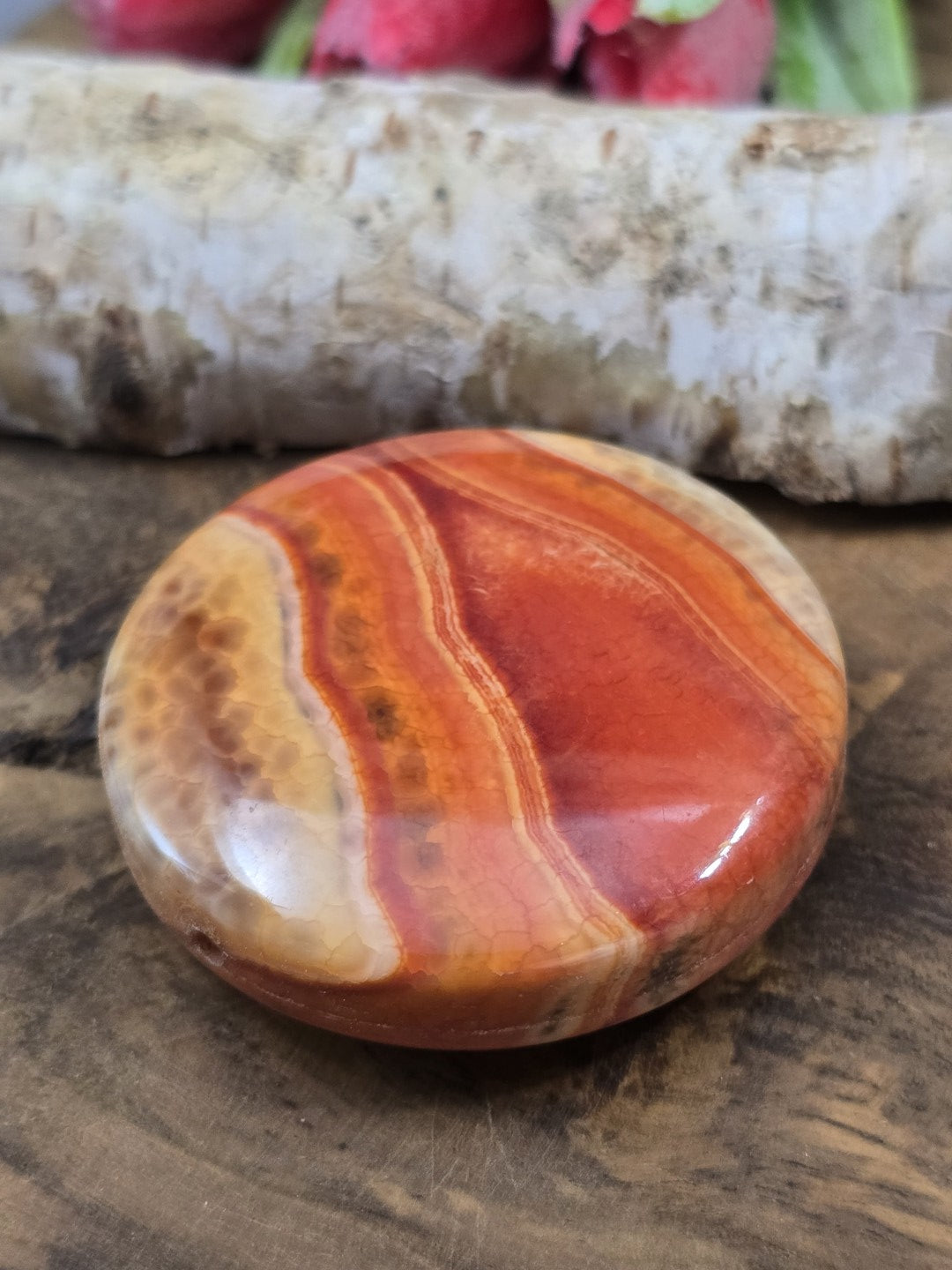 Schräge Draufsicht der flachen rot-orangen Achatperle mit glänzend polierter Oberfläche und Bänderung.