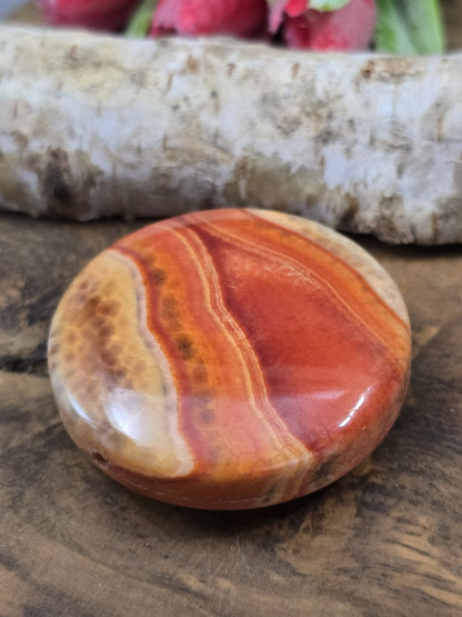 Schräge Draufsicht der flachen rot-orangen Achatperle mit glänzend polierter Oberfläche und Bänderung.