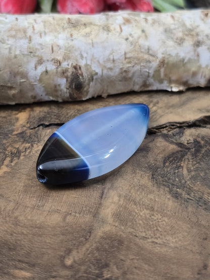 Liegende blaue Achatperle in Navette-Form auf Holz zur Verdeutlichung der Wölbung und der seitlichen Fädelbohrung.