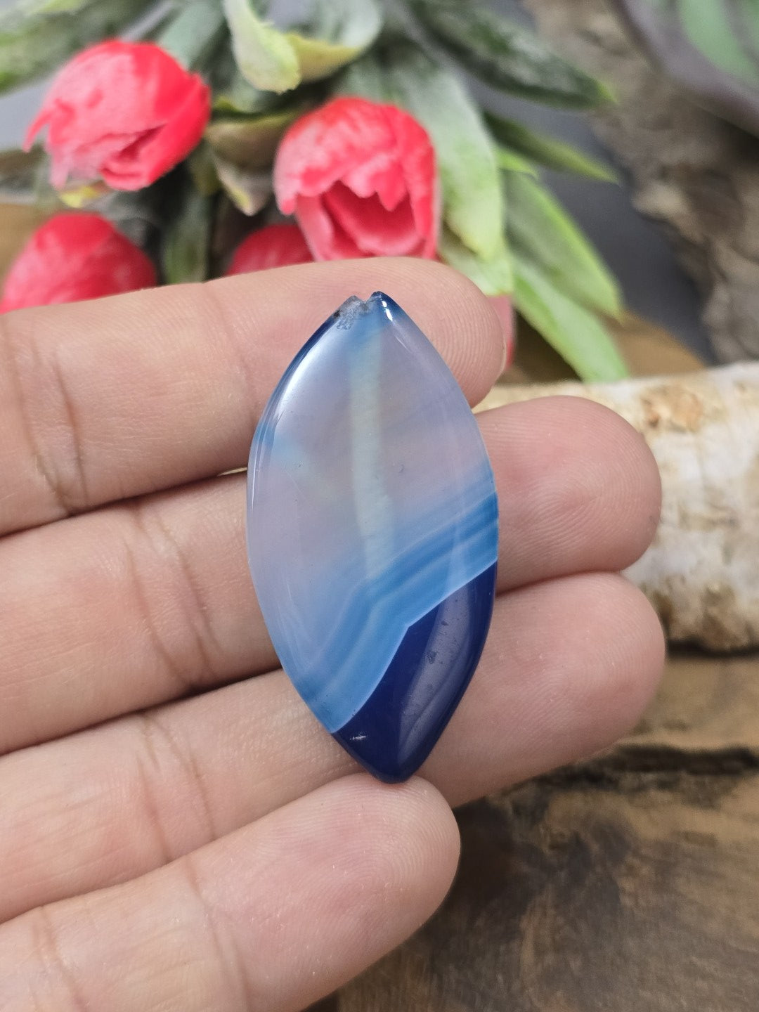 Große blau gebänderte Achat-Navetteperle (39 mm) auf einer Handfläche als präziser Größenvergleich für die Schmuckherstellung.
