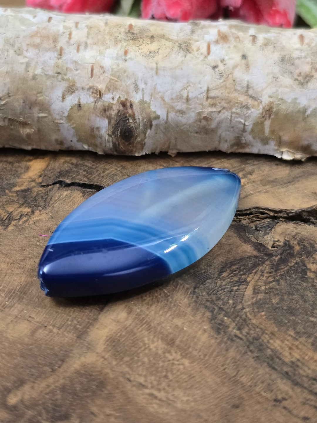 Liegende blaue Achat-Navetteperle auf Holz zur Darstellung der Wölbung und polierten Oberfläche der Centerperle.