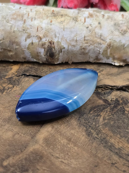 Liegende blaue Achat-Navetteperle auf Holz zur Darstellung der Wölbung und polierten Oberfläche der Centerperle.