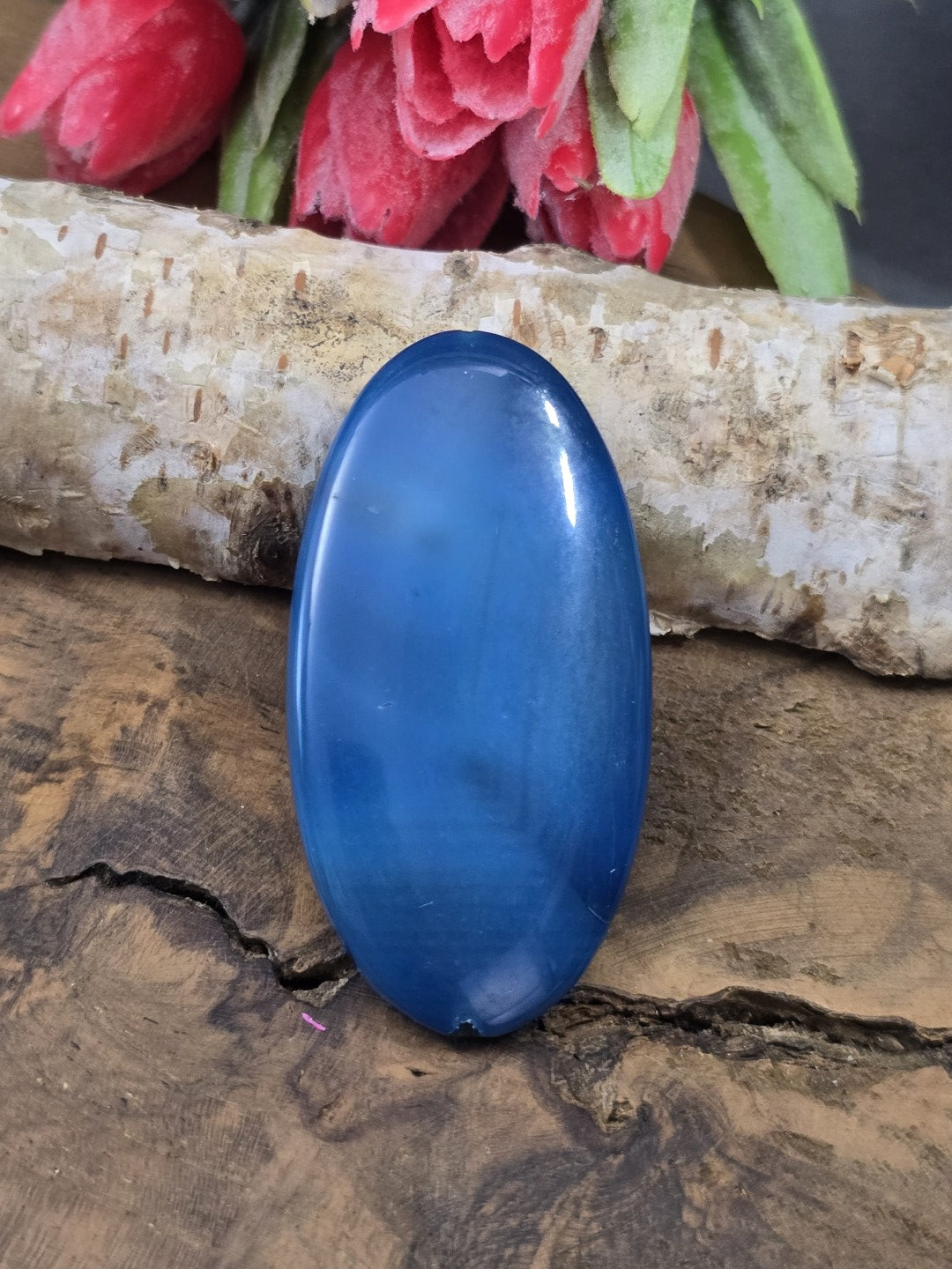 Blaue Achat-Centerperle (50 mm) in Navette-Form mit kräftiger blauer Färbung auf Holz vor Birkenstamm.