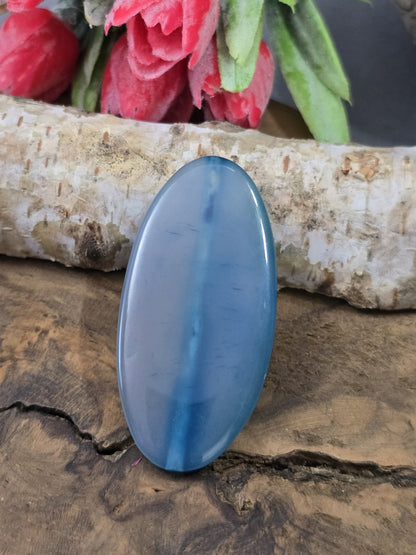 Blaue Achat-Centerperle (51 mm) in Navette-Form mit dezenter Streifenmaserung auf Holz vor Birkenstamm.