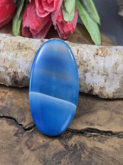 Blau gebänderte Achat-Centerperle (48 mm) in Navette-Form mit weißer Linie auf Holz vor Birkenstamm.
