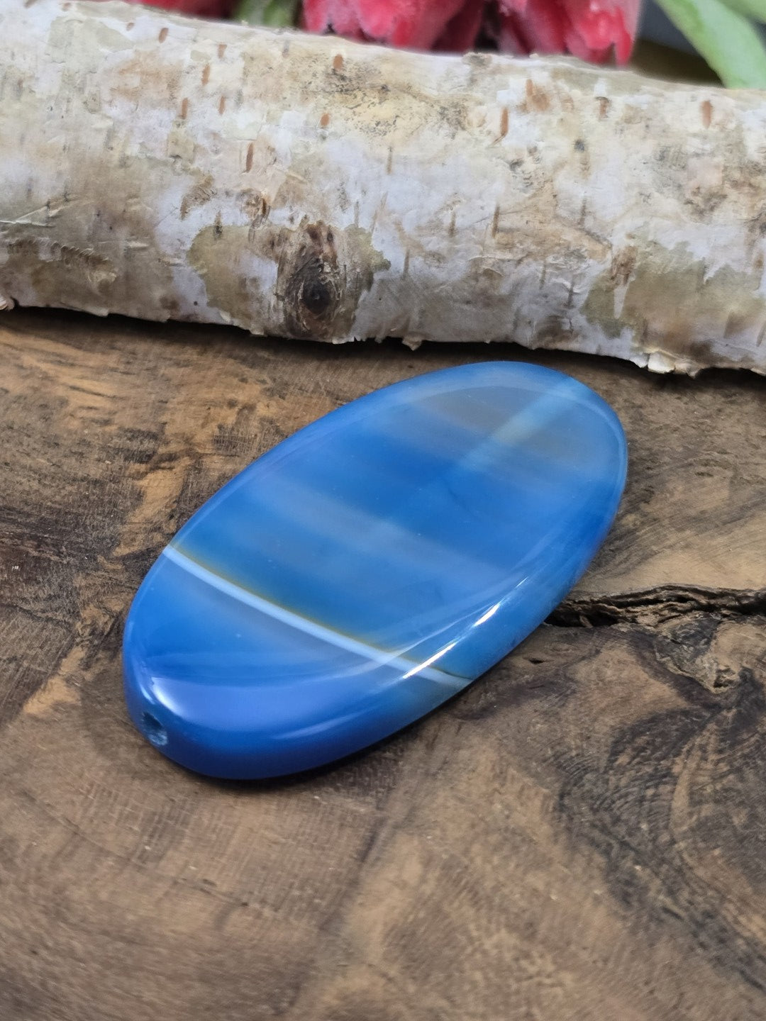 Liegende blau gebänderte Achat-Centerperle (48 mm) auf Holz zur Darstellung der flachen Wölbung und Fädelbohrung.