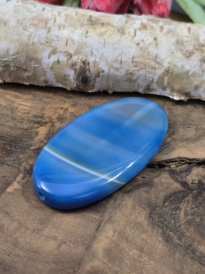 Liegende blau gebänderte Achat-Centerperle (48 mm) auf Holz zur Darstellung der flachen Wölbung und Fädelbohrung.