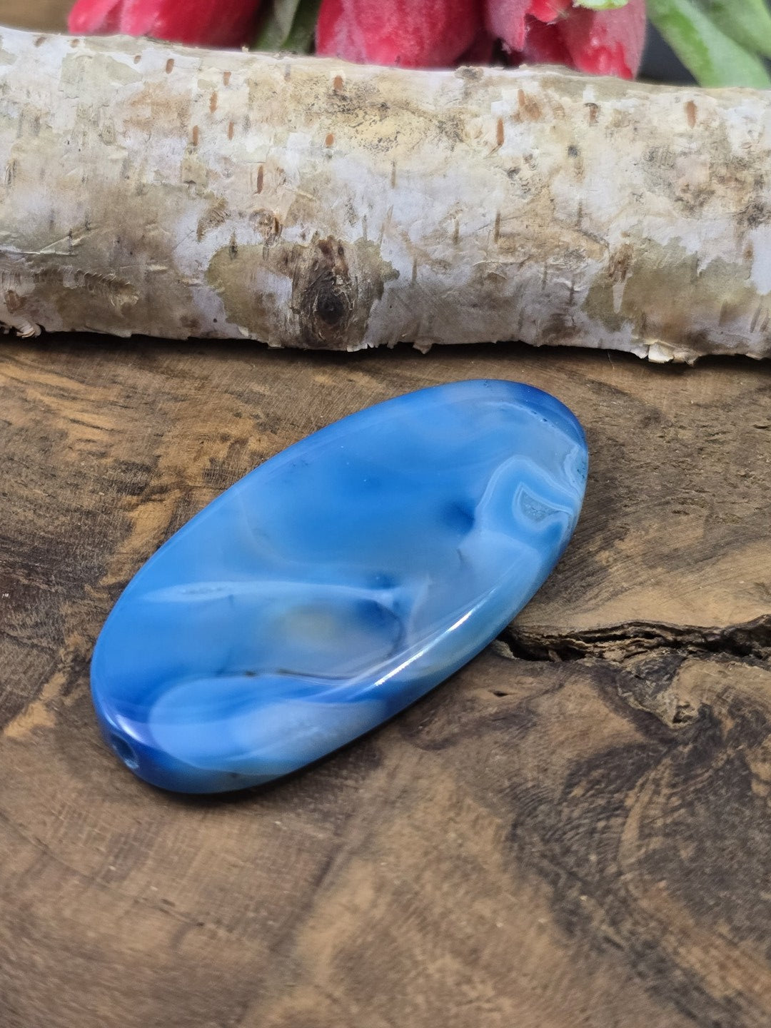 Liegende blau gemusterte Achat-Centerperle (50 mm) auf Holz zur Darstellung der flachen Wölbung und Fädelbohrung.