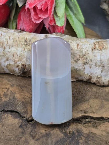 Hellgraue, semitransparente Achat-Centerperle (49 mm) in Pillow-Rechteckform vor Birkenstamm und roten Blüten.
