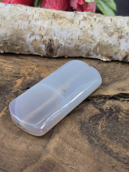Liegende hellgraue Achat-Centerperle (49 mm) auf Holz zur Darstellung der Transparenz und inneren Äderung.