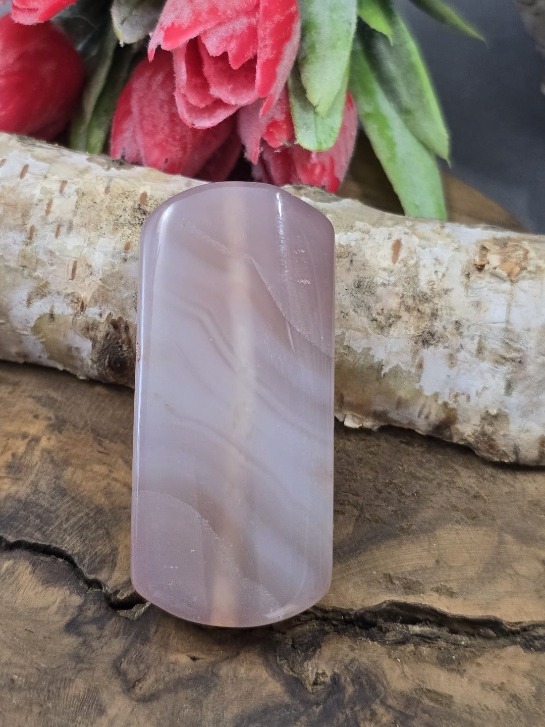 Zartrosa Achat-Centerperle (50 mm) in Pillow-Rechteckform mit feiner Bänderung vor Birkenstamm und roten Blüten.