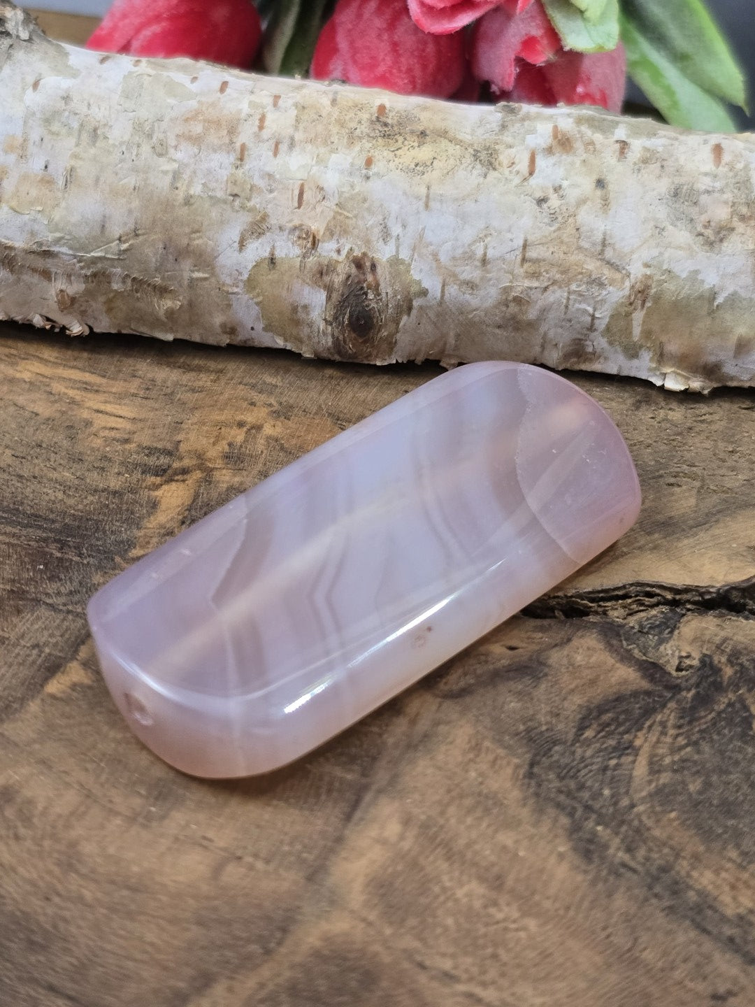 Liegende zartrosa Achat-Centerperle (50 mm) auf Holz zur Darstellung der flachen Form und Fädelbohrung.