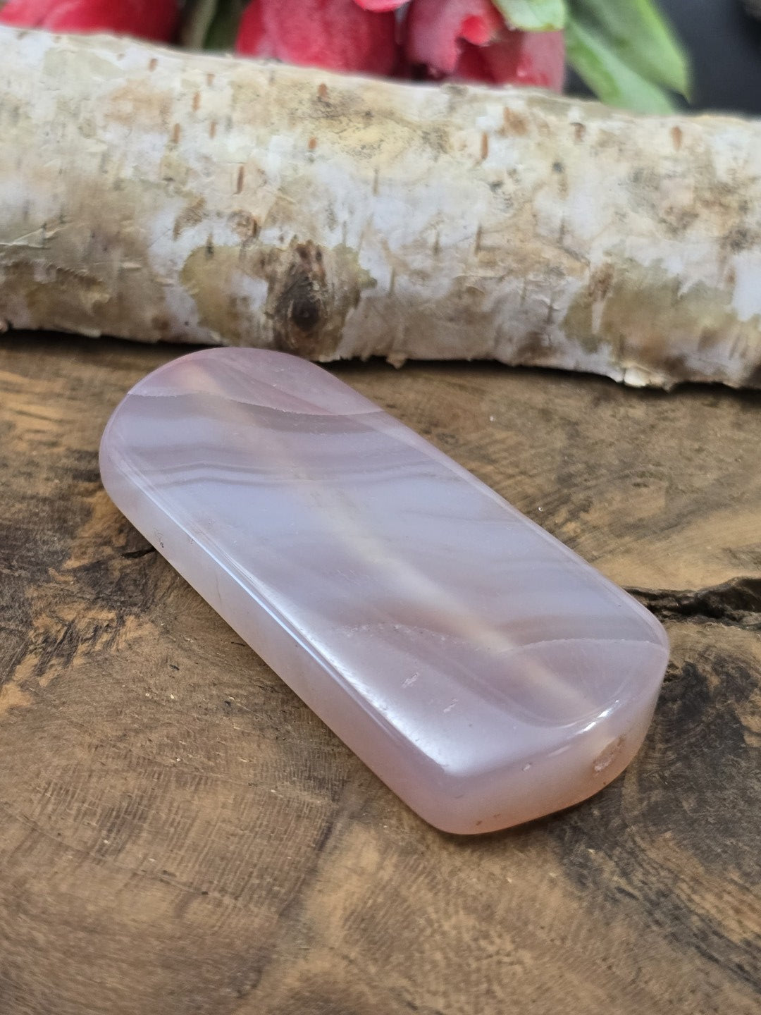Seitliche Perspektive der flach liegenden zartrosa Achat-Pillowperle mit sichtbarem Loch-Eingang der Längsbohrung.