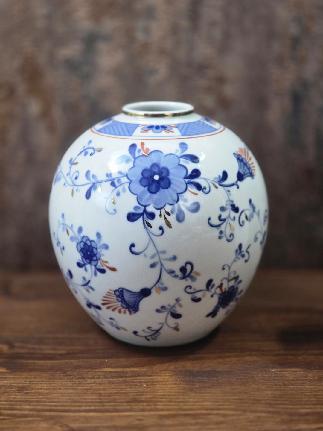 Vintage Porzellanvase in Kugelform mit blauem Blumendekor, Goldakzenten und schmalem Goldrand, frontal auf einem Holztisch fotografiert