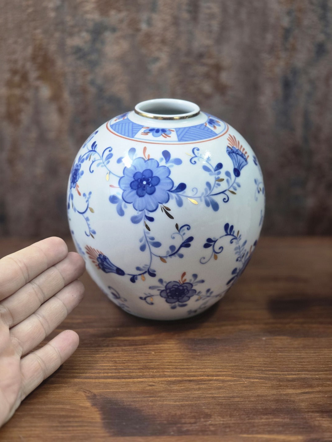 Vintage Kugelvase aus Porzellan mit blauem Floraldekor und Goldakzenten, neben einer Hand zur Darstellung der Größe fotografiert
