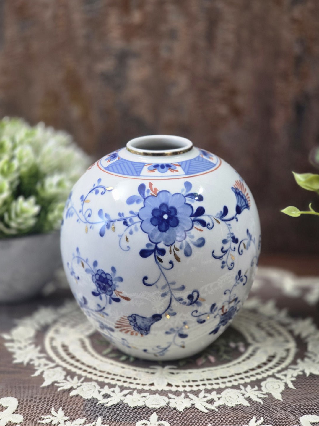 Vintage Kugelvase mit blauem Blumendekor, Goldakzenten und weißem Porzellan, dekorativ auf einer Spitzendecke arrangiert