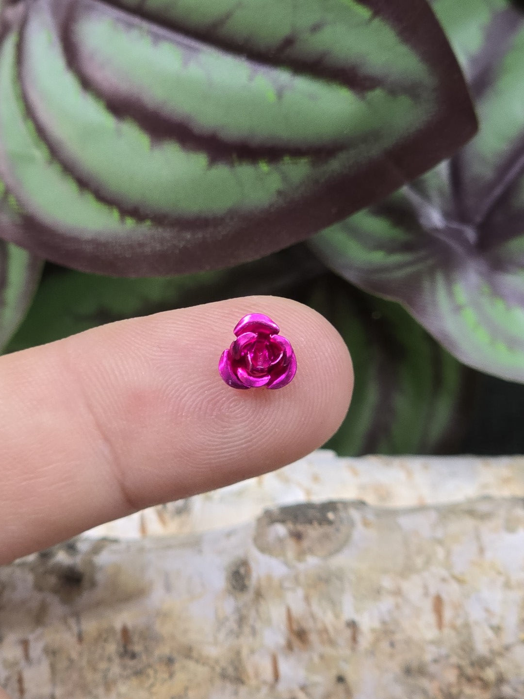 Kleine rosa Aluminium-Rosenperle 7 mm als Größenvergleich auf der Fingerspitze
