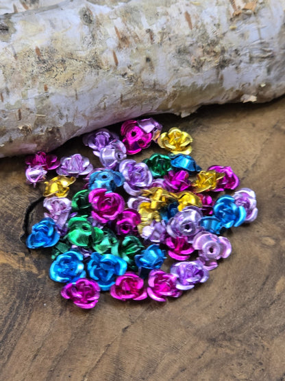 Bunter Haufen Alu-Rosenperlen in Pink, Blau, Grün, Violett und Gold auf Holzgrund