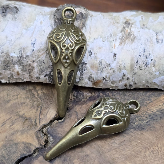 Das Bild zeigt einen detaillierten Krähenschädel mit Intarsien, gehalten in antik bronzefarbenem Finish. Er ist einseitig geprägt und hat eine hohle Rückseite, was ihn leicht und vielseitig macht.