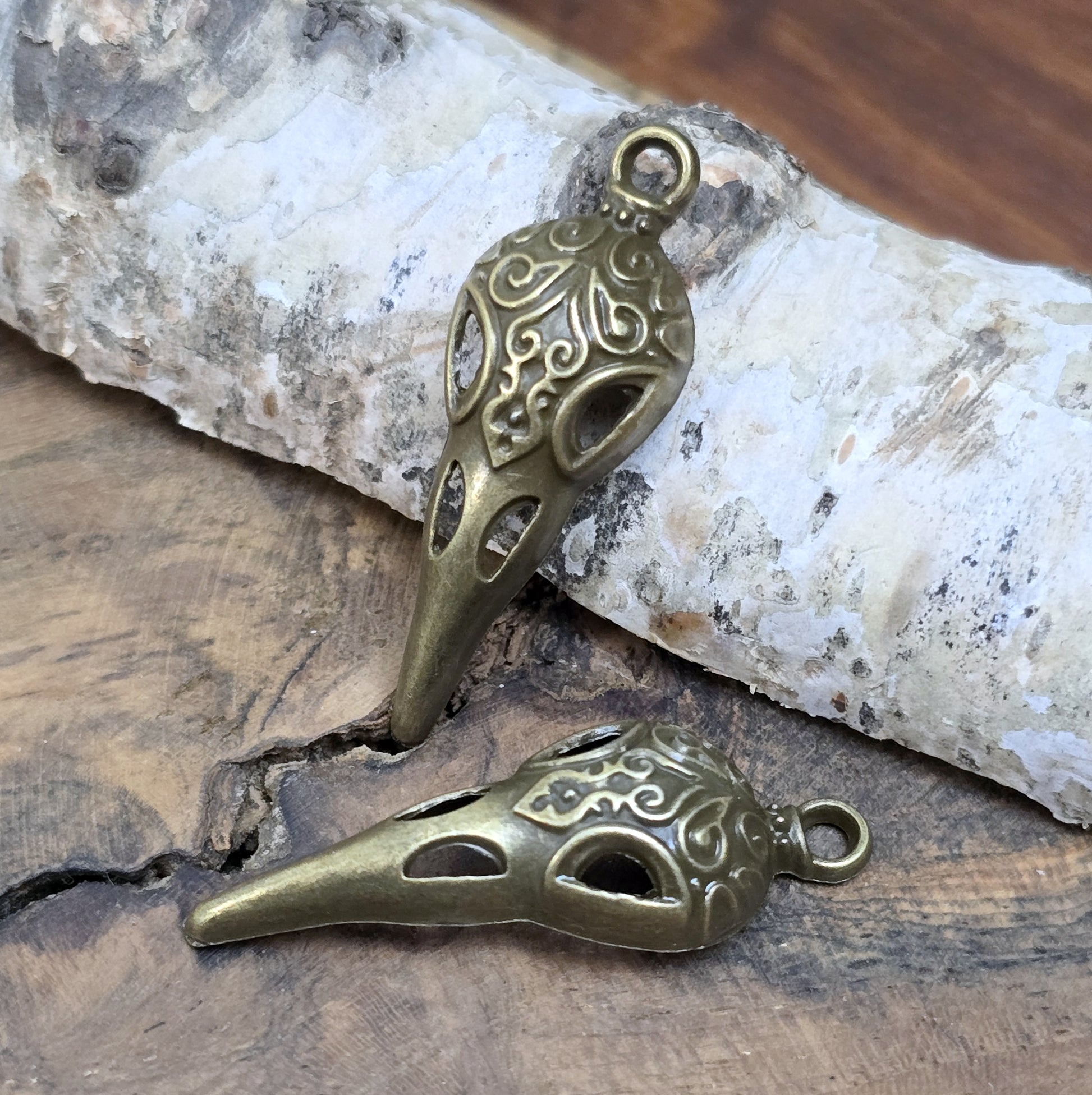 Das Bild zeigt einen detaillierten Krähenschädel mit Intarsien, gehalten in antik bronzefarbenem Finish. Er ist einseitig geprägt und hat eine hohle Rückseite, was ihn leicht und vielseitig macht.