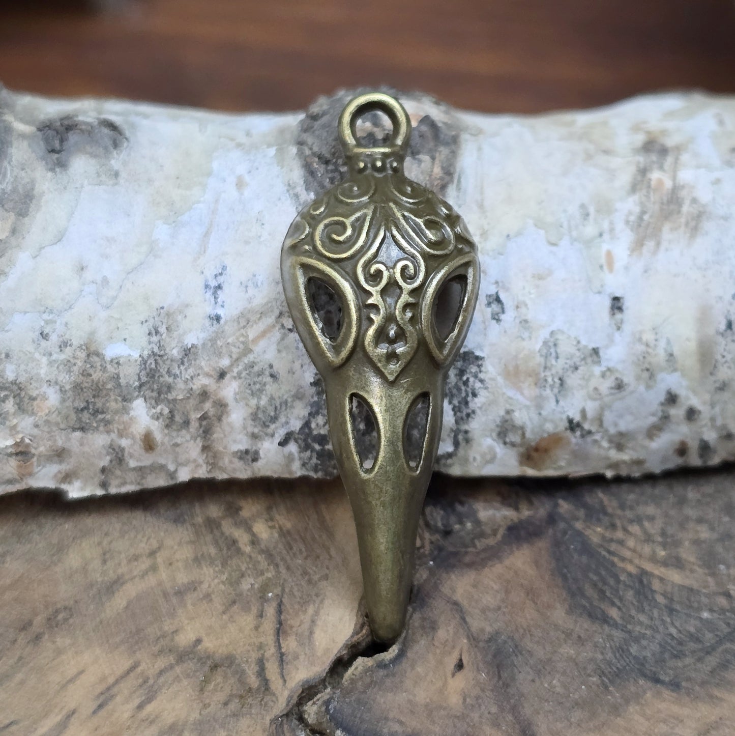Das Bild zeigt einen detaillierten Krähenschädel mit Intarsien, gehalten in antik bronzefarbenem Finish. Er ist einseitig geprägt und hat eine hohle Rückseite, was ihn leicht und vielseitig macht.