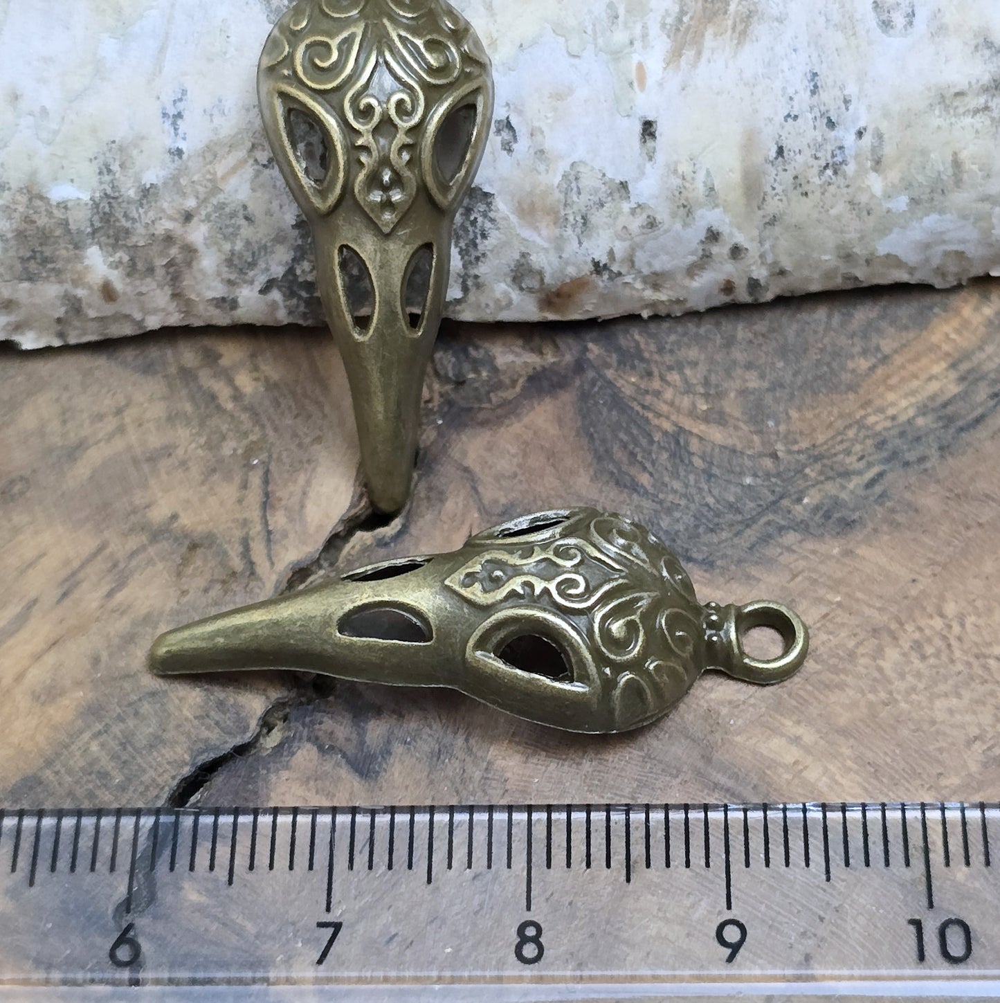 Das Bild zeigt einen detaillierten Krähenschädel mit Intarsien, gehalten in antik bronzefarbenem Finish. Er ist einseitig geprägt und hat eine hohle Rückseite, was ihn leicht und vielseitig macht.