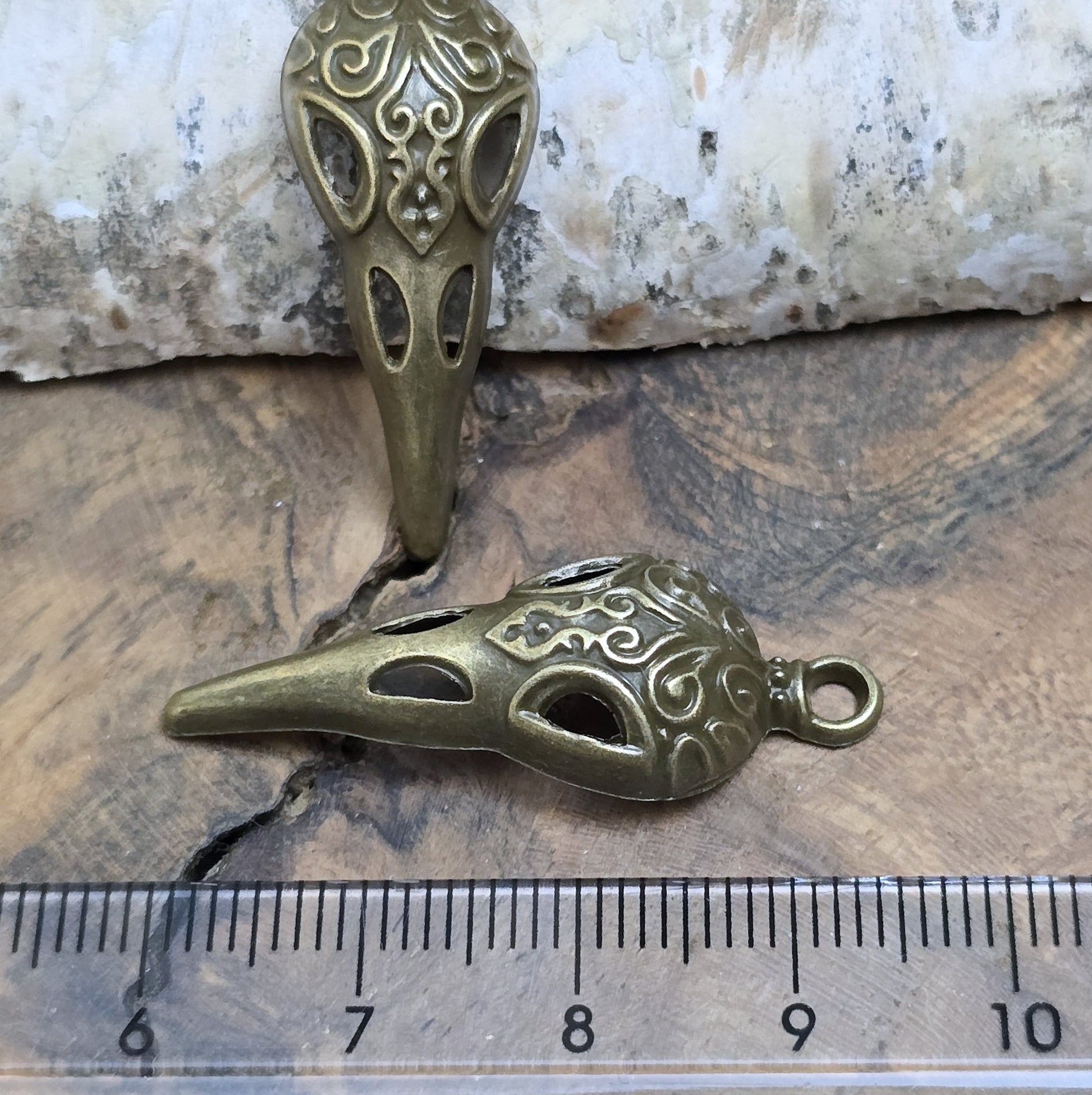 Das Bild zeigt einen detaillierten Krähenschädel mit Intarsien, gehalten in antik bronzefarbenem Finish. Er ist einseitig geprägt und hat eine hohle Rückseite, was ihn leicht und vielseitig macht.