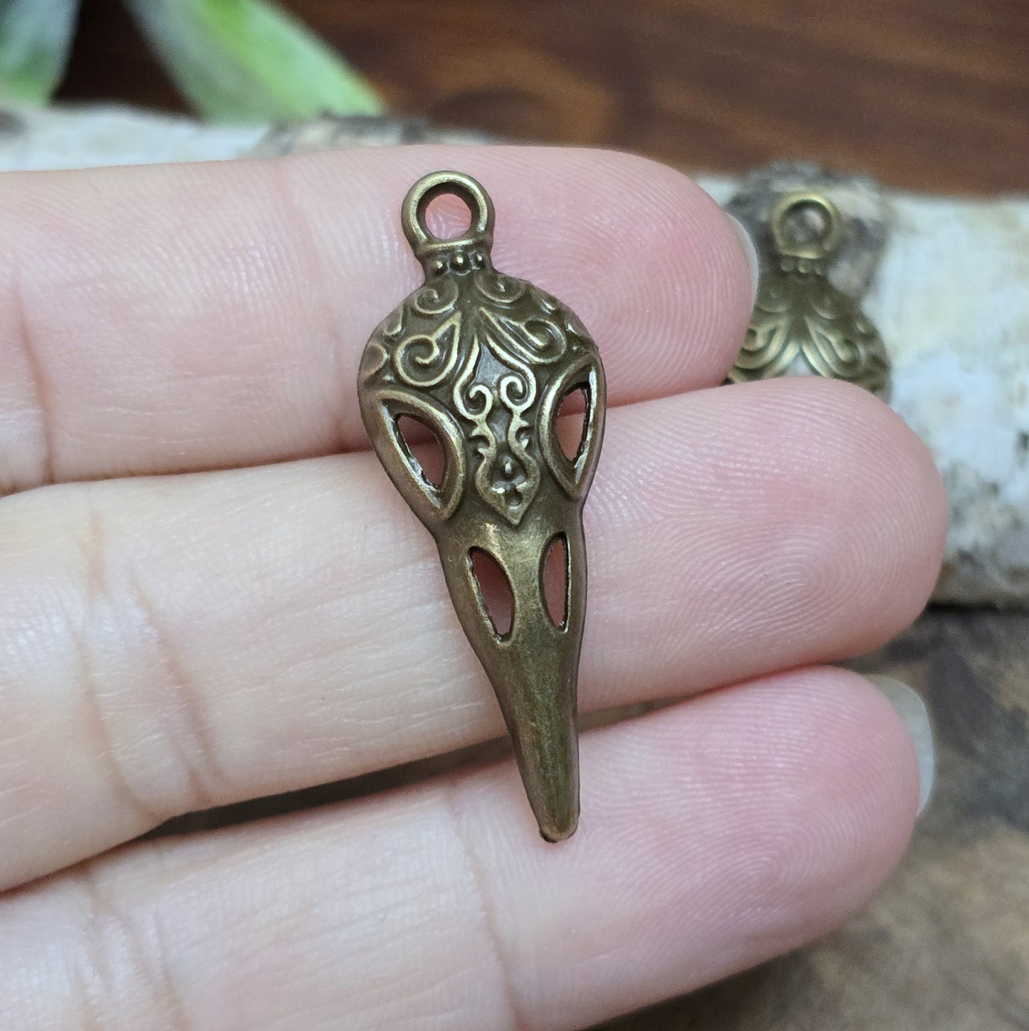 Das Bild zeigt einen detaillierten Krähenschädel mit Intarsien, gehalten in antik bronzefarbenem Finish. Er ist einseitig geprägt und hat eine hohle Rückseite, was ihn leicht und vielseitig macht.