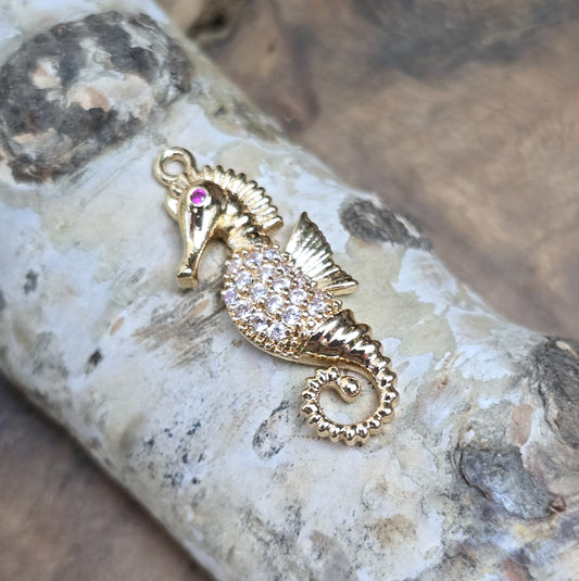 Das Bild zeigt einen eleganten Charms-Anhänger aus Messing, veredelt mit 24 Karat Vergoldung und funkelnden Strasssteinen. Das Seepferdchen, Symbol für Anmut und das Meer, wird hier in seiner ganzen Schönheit hervorgehoben.