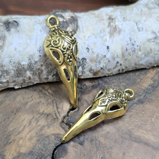 Das Bild zeigt einen detaillierten Krähenschädel mit Intarsien, gehalten in antik goldfarbenem Finish. Er ist einseitig geprägt und hat eine hohle Rückseite, was ihn leicht und vielseitig macht.
