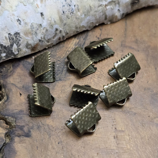 Bandklemme mit Zähnen, antik bronzefarbig, 8 mm breit. Ideal zum Befestigen von Verschlüssen an Stoffbändern. Einfach mit einer Zange am Bandende fixieren – für sicheren Halt und eine dekorative Optik.