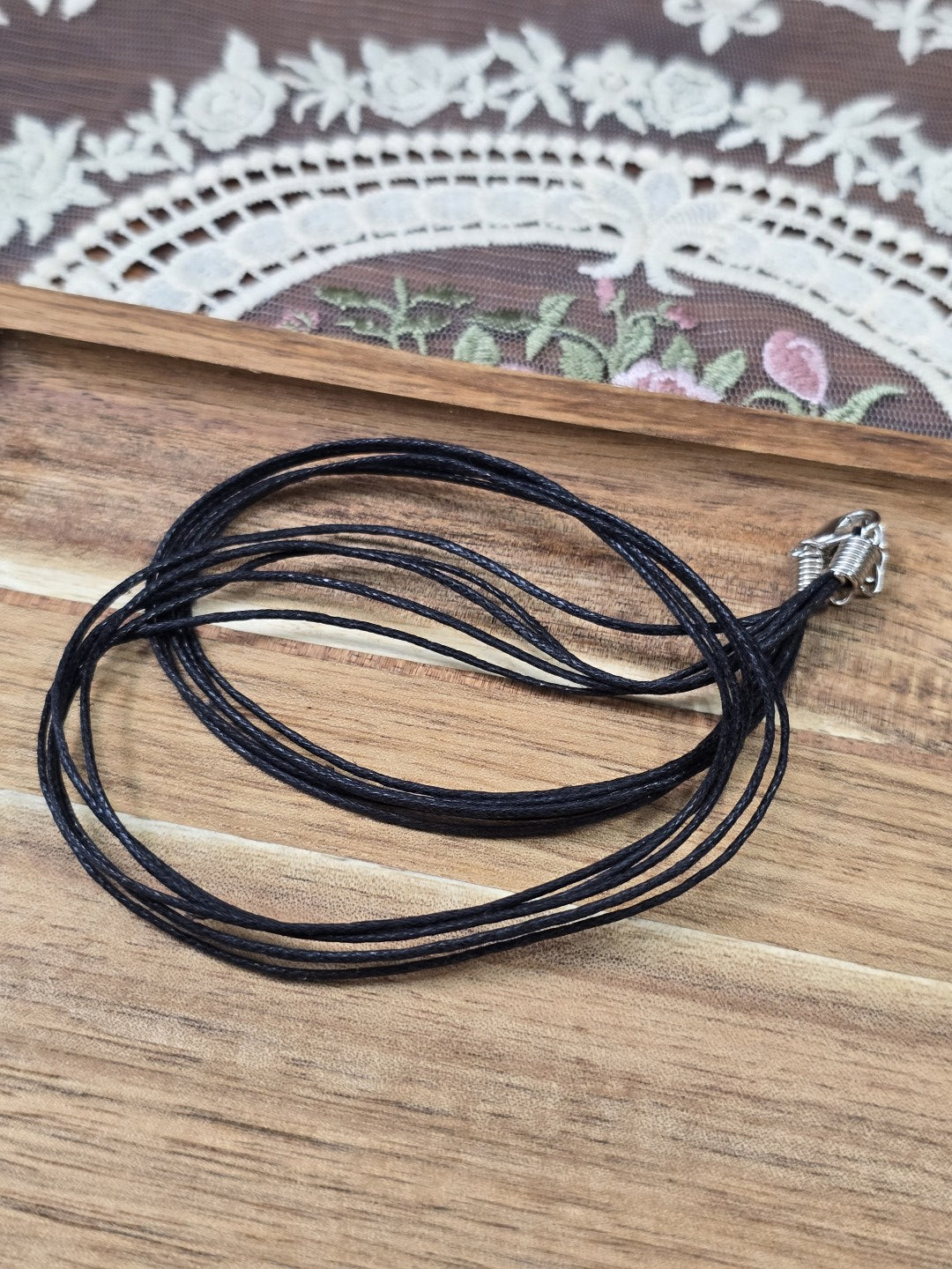 5-fädige schwarze Baumwollkette als Schmuckbasis zusammengerollt auf Holzgrund.