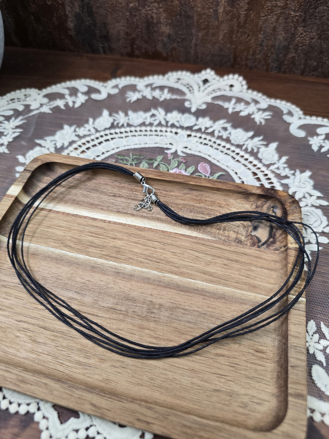 Schwarze Baumwollkette 42cm mit Silber-Karabinerverschluss und Verlängerungskette ausgelegt auf Holztablett.