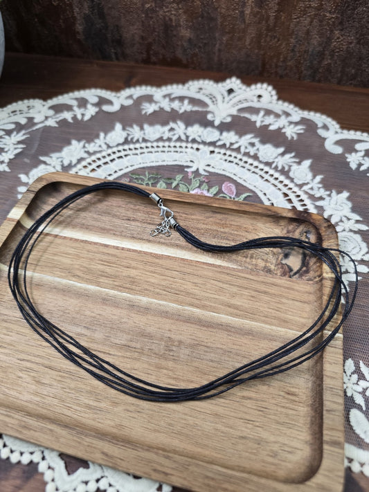 Schwarze Baumwollkette 42cm mit Silber-Karabinerverschluss und Verlängerungskette ausgelegt auf Holztablett.