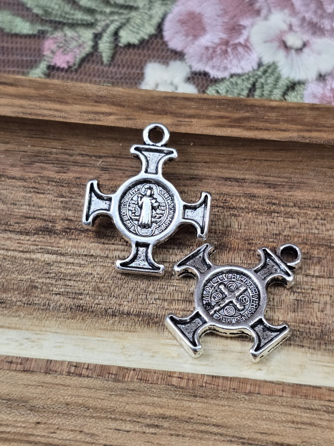 Zwei Benediktus-Kreuz-Anhänger in Antiksilber von Vorder- und Rückseite auf Holzgrund.